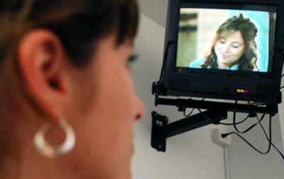Imagen del rostro de perfil de una mujer observando la pantalla de un televisor otra mujer sonriendo.